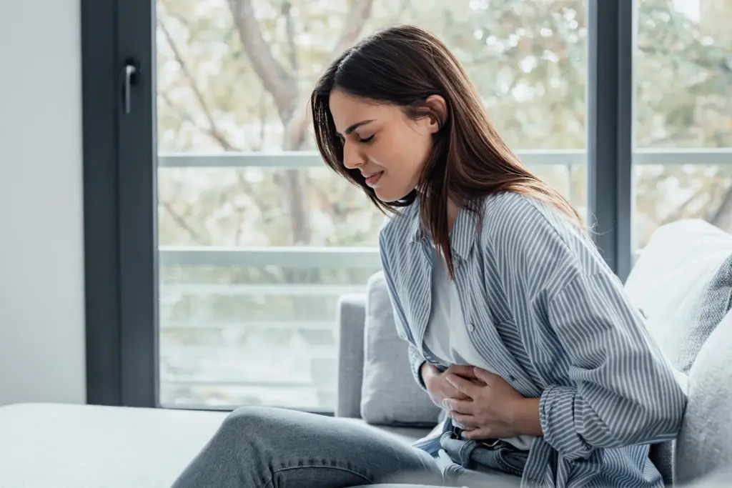 A woman sitting by a window holding her stomach with both hands