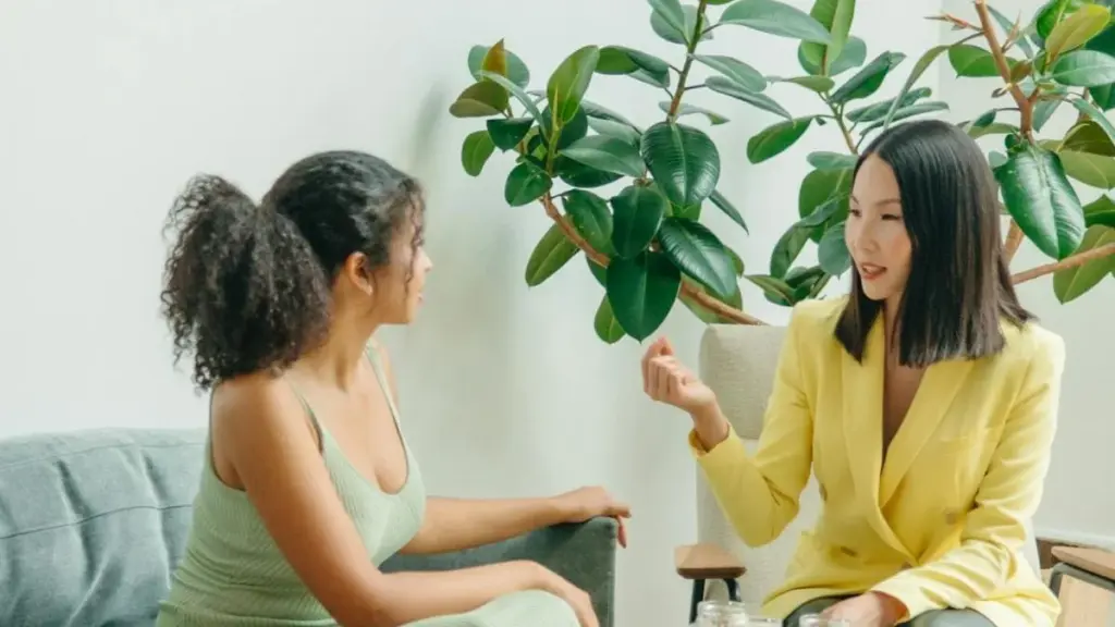 Two women in conversation in a calm room with a large indoor plant