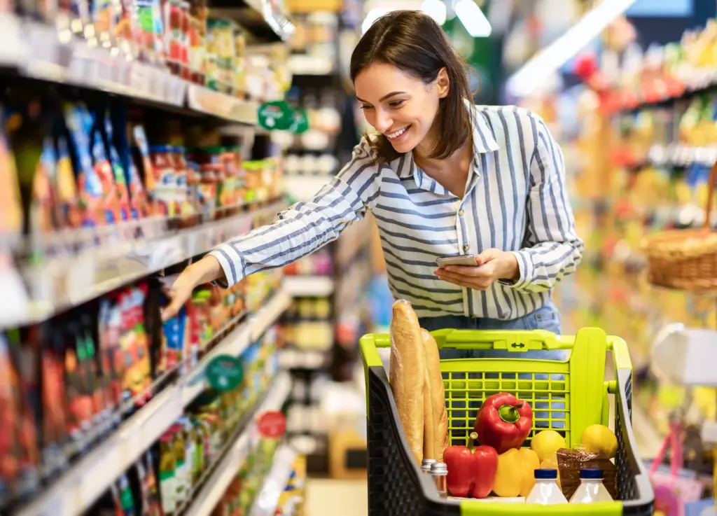 A woman shopping in a supermarket aisle with a basket of fresh fruit and vegetables