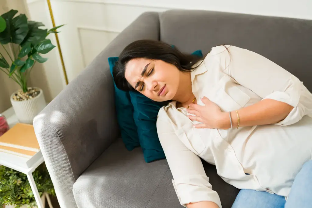 A woman lying on a couch with a hand on her chest, uncomfortable with reflux