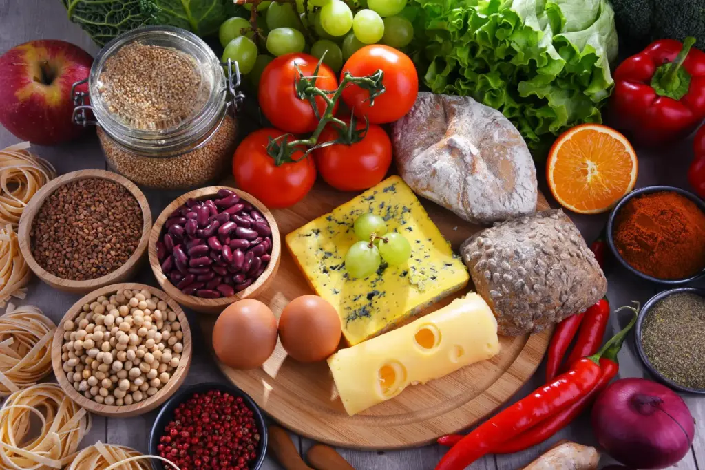 An overhead view of varied whole foods including eggs, cheese, legumes, grains, wholegrain bread, tomatoes and fresh vegetables