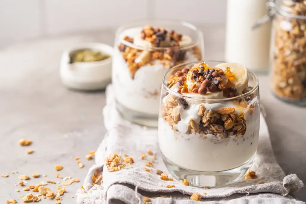 Two glass jars of yoghurt layered with oat granola and banana