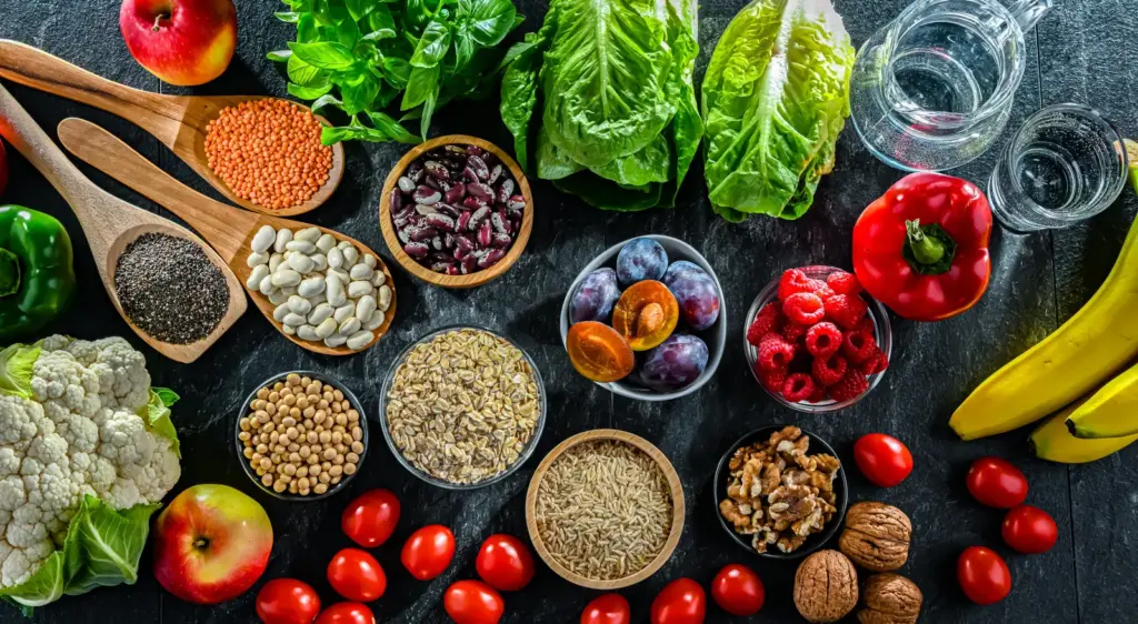 Bowls of legumes, grains, seeds, nuts, fruit and vegetables on a dark table